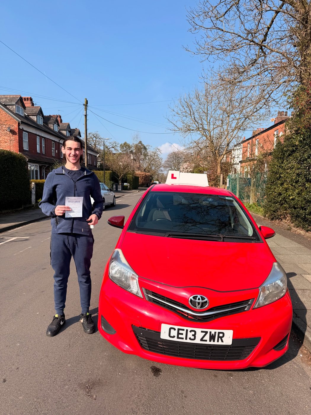 Student celebrating a driving test pass with learner car